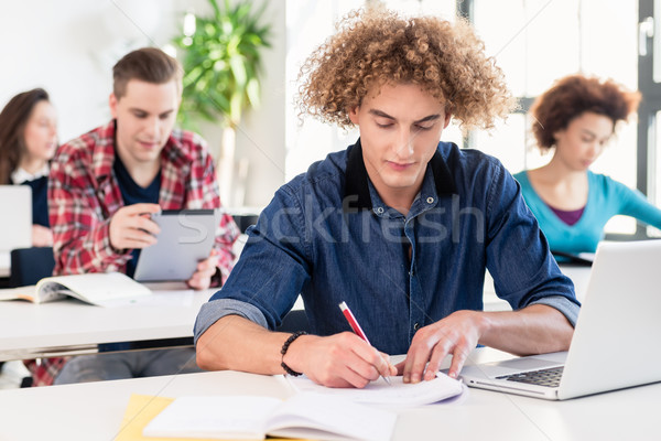 Portrait of a young hard-working student writing during class in Stock photo © Kzenon