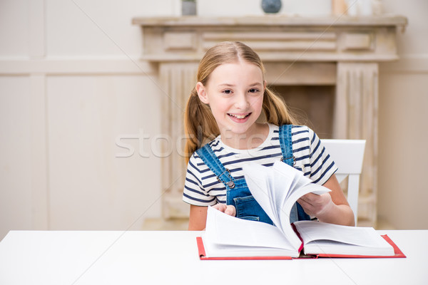 Cute preteen girl sitting at table with book and smiling at camera Stock photo © LightFieldStudios