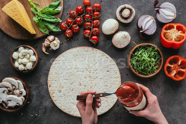 cropped shot of woman spreading ketchup onto raw pizza dough on concrete table Stock photo © LightFieldStudios