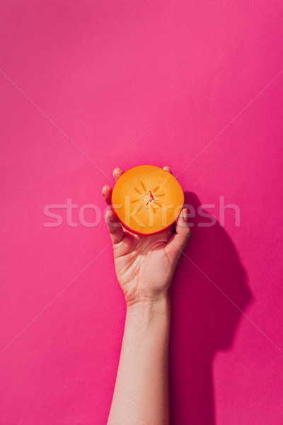 elevated view of woman holding persimmon piece on pink Stock photo © LightFieldStudios