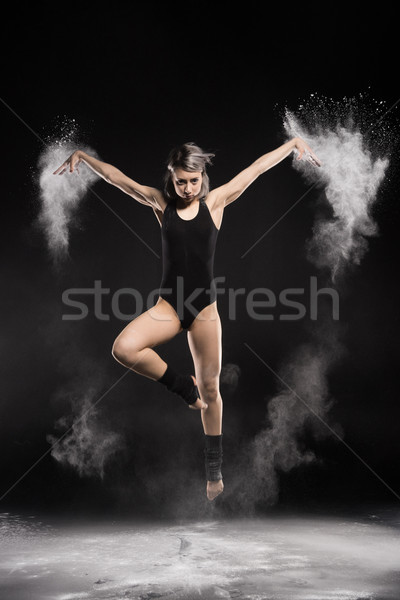 concentrated woman in bodysuit with dust jumping on black Stock photo © LightFieldStudios