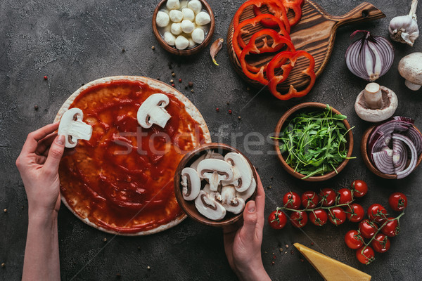 cropped shot of woman spreading mushroom slices onto pizza on concrete table Stock photo © LightFieldStudios