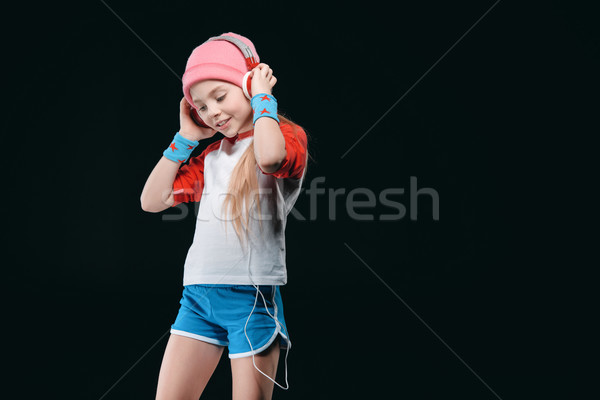 Smiling little girl in sportswear wearing headphones and posing isolated on black, activities for ch Stock photo © LightFieldStudios