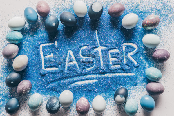 top view of easter sign made of blue sand with painted eggs on white Stock photo © LightFieldStudios