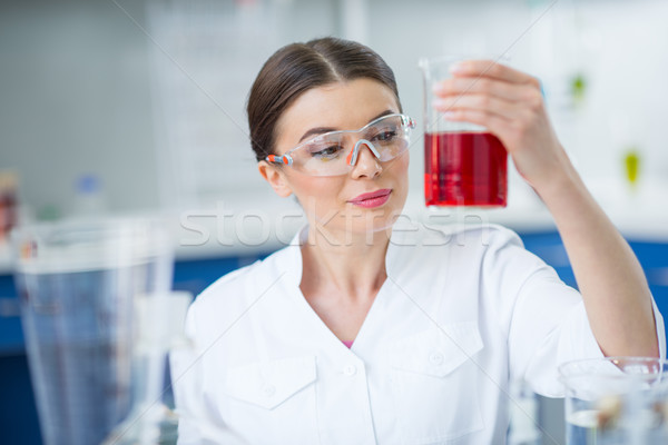 Smiling woman scientist in protective workwear holding flask with reagent in lab Stock photo © LightFieldStudios