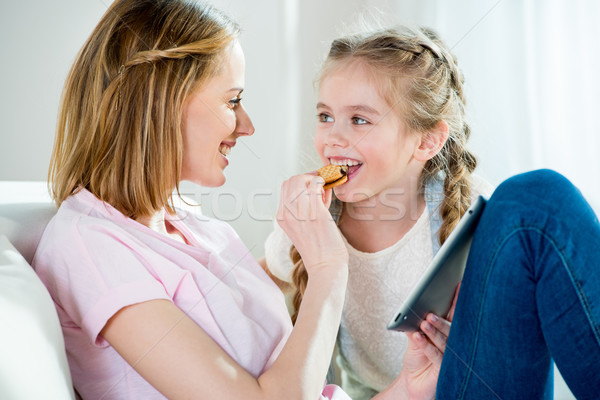 Happy mother feeding daughter with cookie while using digital tablet Stock photo © LightFieldStudios