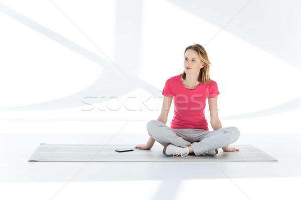 Young pensive woman sitting on yoga mat with smartphone and looking away Stock photo © LightFieldStudios