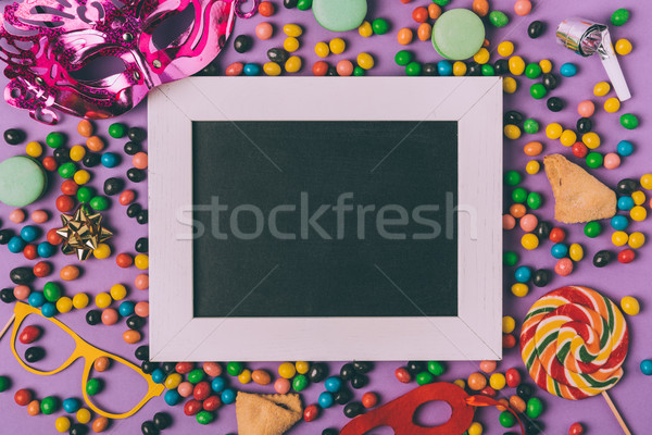 Stock photo: top view of arranged masquerade masks, candies, cookies and empty blackboard isolated on purple