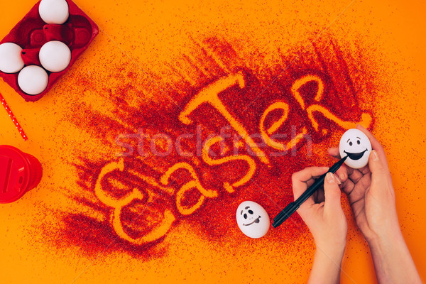 cropped image of woman painting smileys on easter eggs on orange Stock photo © LightFieldStudios