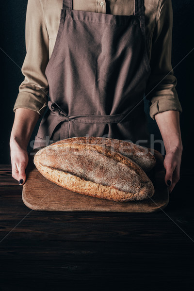 partial view of woman holding loafs of bread on wooden cutting board isolated on black Stock photo © LightFieldStudios