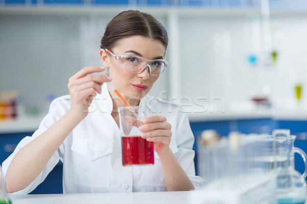 Woman scientist in protective goggles holding flask with reagent and pipette in lab Stock photo © LightFieldStudios