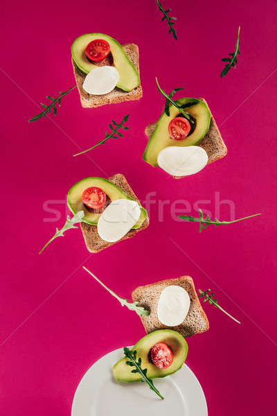 close up view of toasts, avocado pieces, mozzarella cheese and cherry tomatoes falling on plate isol Stock photo © LightFieldStudios