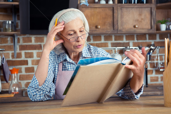 Idős nő szakácskönyv szemüveg olvas konyha Stock fotó © LightFieldStudios