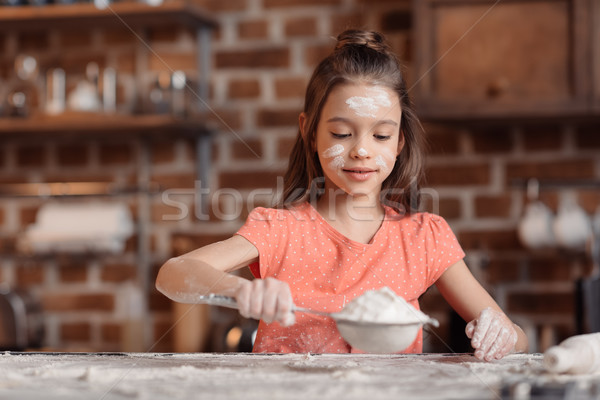 'Cute little girl with flour on face sifting flour at kitchen table Stock photo © LightFieldStudios