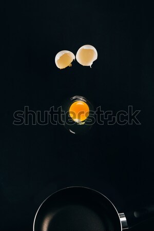 close up view of raw egg yolk falling on frying pan isolated on black Stock photo © LightFieldStudios