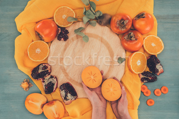 cropped image of woman holding two pieces of persimmon Stock photo © LightFieldStudios