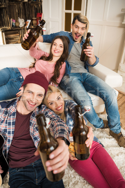 Happy young friends with beer bottles smiling at camera at home Stock photo © LightFieldStudios