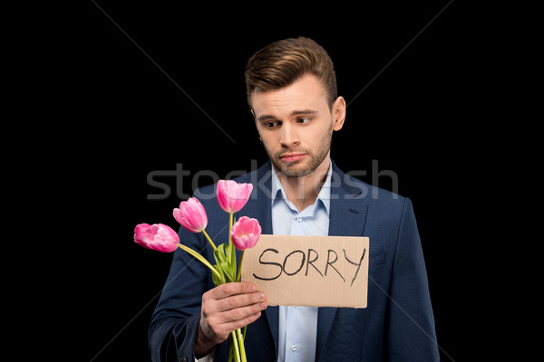 Upset young man holding pink tulips bouquet and sorry sign on black  Stock photo © LightFieldStudios