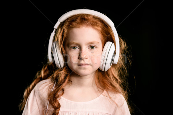 portrait of adorable redhead girl listening music with headphones looking at camera isolated on blac Stock photo © LightFieldStudios