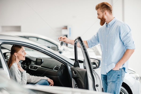 Stock photo: Man giving car key to woman sitting in car in dealership salon   