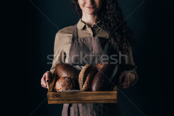 cropped shot of smiling woman holding wooden box with loafs of bread in hands isolated on black Stock photo © LightFieldStudios