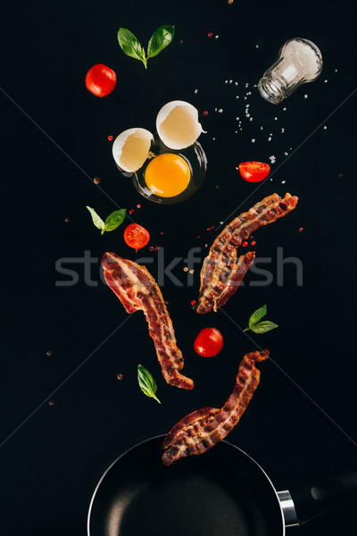 close up view of pieces of bacon, cherry tomatoes and raw egg yolk falling on frying pan isolated on Stock photo © LightFieldStudios