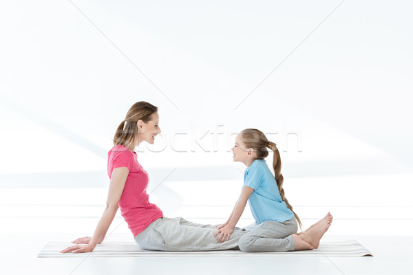 Side view of happy mother and daughter sitting on yoga mat and looking at each other Stock photo © LightFieldStudios