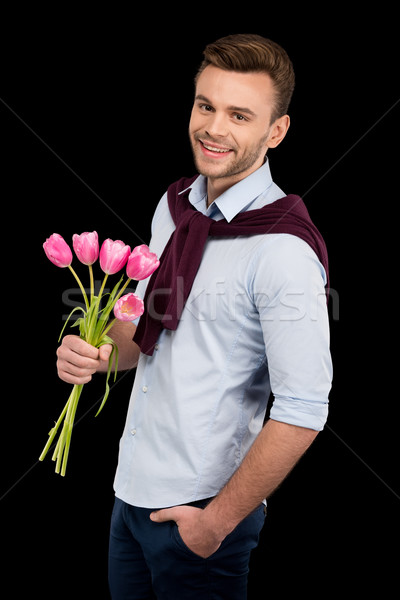 Handsome young man with hand in pocket holding tulips and smiling at camera, international womens da Stock photo © LightFieldStudios