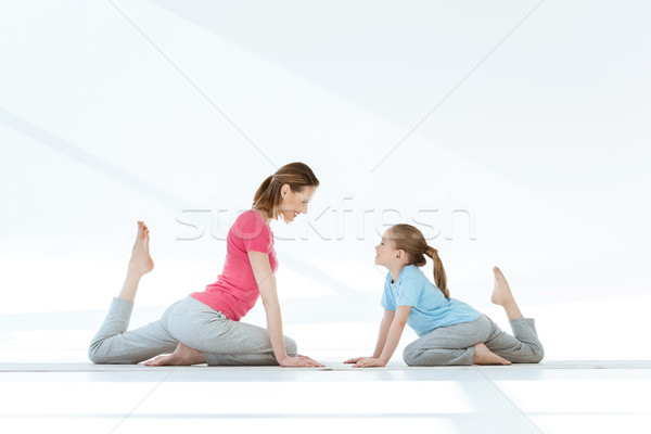 Smiling mother and daughter practicing pigeon yoga pose on mats and looking at each other Stock photo © LightFieldStudios