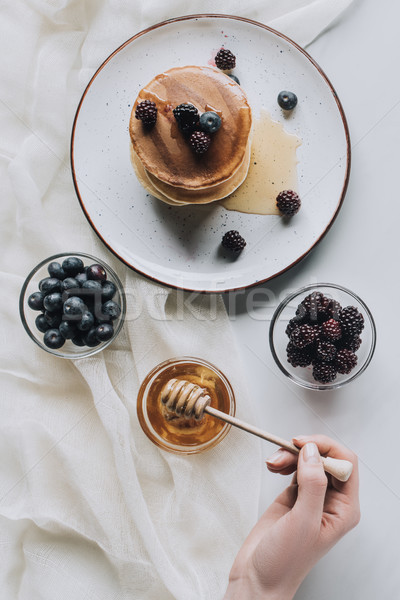 cropped shot of person eating homemade pancakes with fresh berries and honey on grey Stock photo © LightFieldStudios