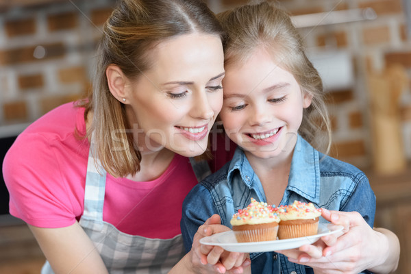 portrait of smiling mother and daughter holding plate with cupcakes Stock photo © LightFieldStudios