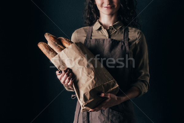 cropped shot of woman in apron holding french baguettes in paper bag in hands isolated on black Stock photo © LightFieldStudios