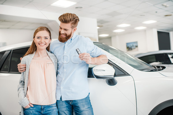 Happy couple holding car key and standing at car in dealership salon    Stock photo © LightFieldStudios