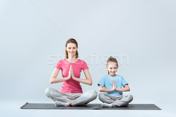 Smiling sporty mother and daughter practicing lotus yoga pose and namaste gesture on white Stock photo © LightFieldStudios