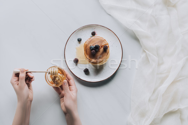 cropped shot of person eating delicious homemade pancakes with berries and honey on grey Stock photo © LightFieldStudios
