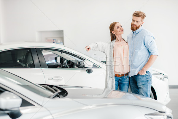 Happy couple choosing car in dealership salon, woman pointing on car Stock photo © LightFieldStudios