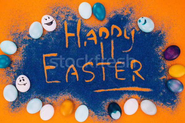 top view of happy easter sign made of blue sand with painted eggs on orange Stock photo © LightFieldStudios