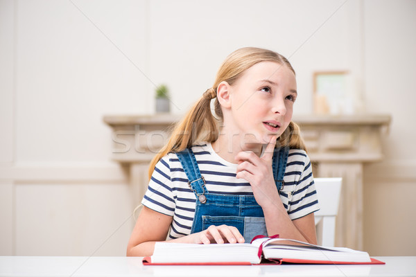 Cute little girl sitting at table with book and thoughtfully looking away Stock photo © LightFieldStudios