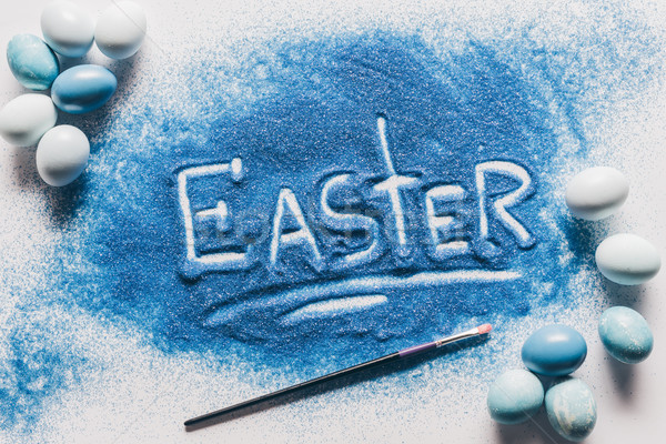 top view of easter sign made of blue sand, brush with painted eggs on white Stock photo © LightFieldStudios