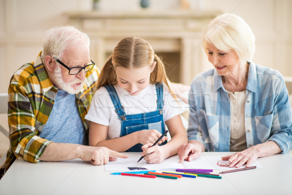 Stock photo: Happy girl with grandfather and grandmother sitting at table and drawing together
