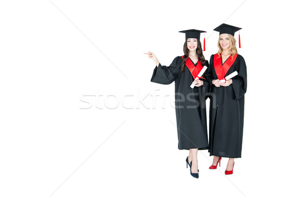Two young smiling women in mantles and mortarboards holding diplomas and pointing away Stock photo © LightFieldStudios