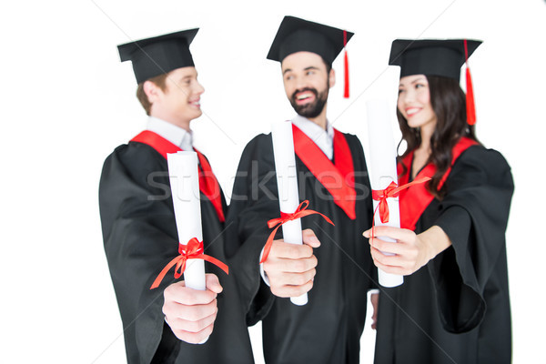 Happy students in graduation caps holding diplomas and smiling each other Stock photo © LightFieldStudios