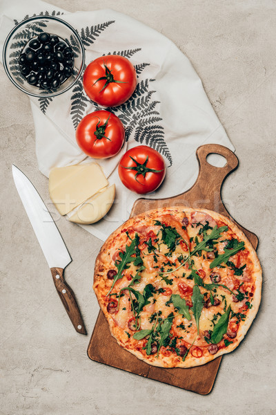 Whole pizza on wooden cutting board with tomatoes, cheese and olives on light background Stock photo © LightFieldStudios