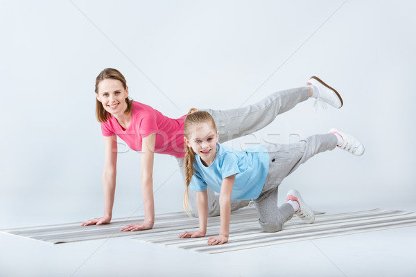 smiling sporty mother and daughter exercising on mats together on white Stock photo © LightFieldStudios