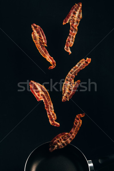 close up view of pieces of bacon falling on frying pan isolated on black Stock photo © LightFieldStudios