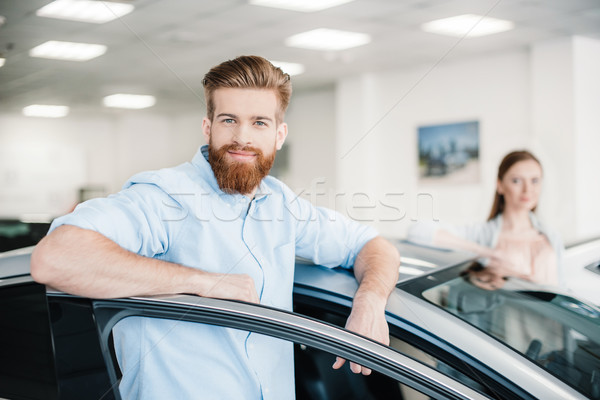 Happy couple standing at car in dealership salon, man looking at camera Stock photo © LightFieldStudios