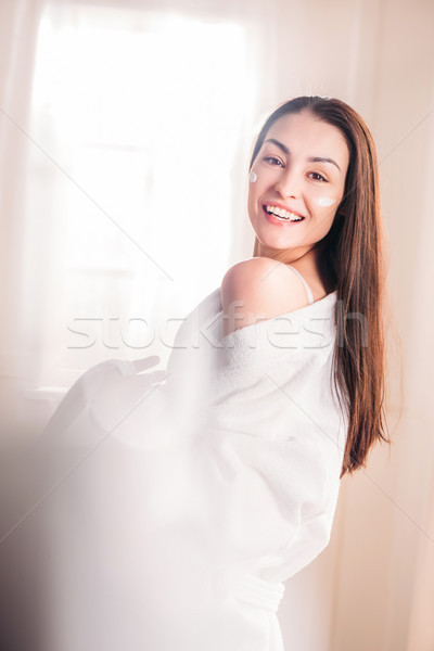 Fiatal nő fürdőköpeny krém arc fiatal nevet Stock fotó © LightFieldStudios