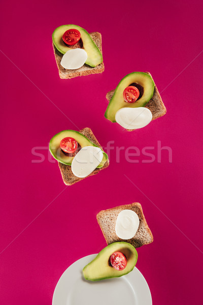 close up view of toasts, avocado pieces, mozzarella cheese and cherry tomatoes falling on plate isol Stock photo © LightFieldStudios