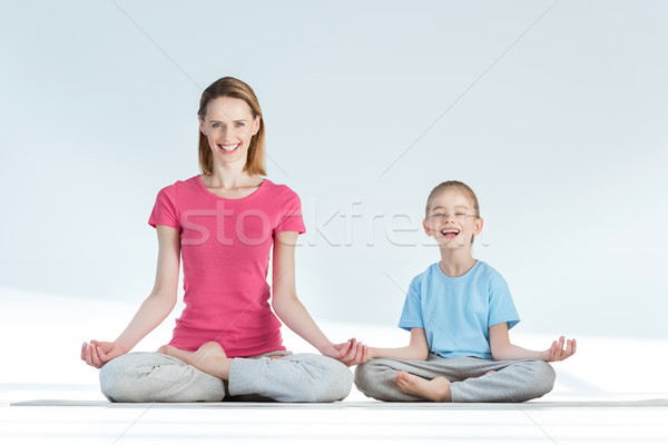 Happy mother and daughter sitting on yoga mat in lotus position and smiling at camera Stock photo © LightFieldStudios