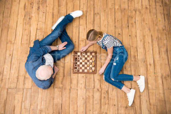Top view of grandfather and granddaughter playing chess on hardwood floor Stock photo © LightFieldStudios